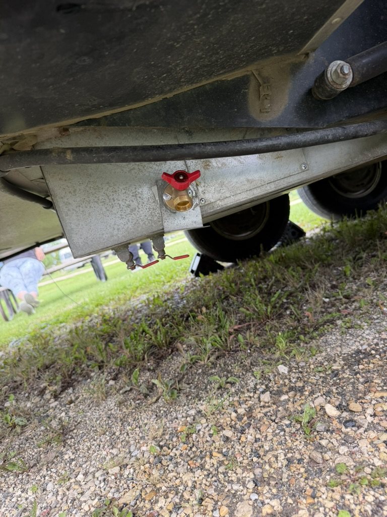 Close view under a trailer of a brass ball valve with a red handle mounted through the belly pan