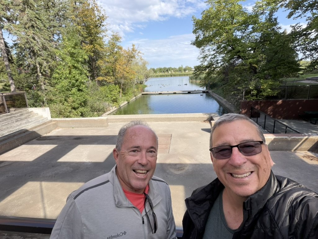 Keith and Steve on the terrace above the Loonie Pond at the Royal Canadian Mint, geese on the water behind them
